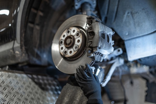 Close up of mechanic's hands wearing gloves, inspecting car brake disc and caliper during maintenance in auto repair shop