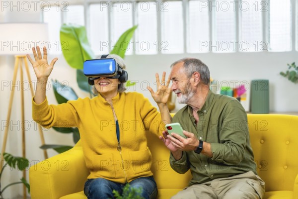 Mature couple having fun together wearing virtual reality glasses and mobile phone sitting on the sofa