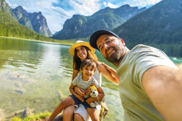 Tourists enjoying summer holidays by a picturesque alpine lake, capturing joyful moments with their child while taking a selfie