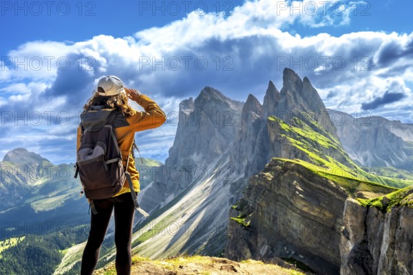 Hiker shielding her eyes while enjoying the breathtaking view of the odle mountain range in the dolomites, italy, during a sunny summer day