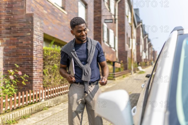 African man opening the car with a remote control on the street on the way to work carrying a laptop
