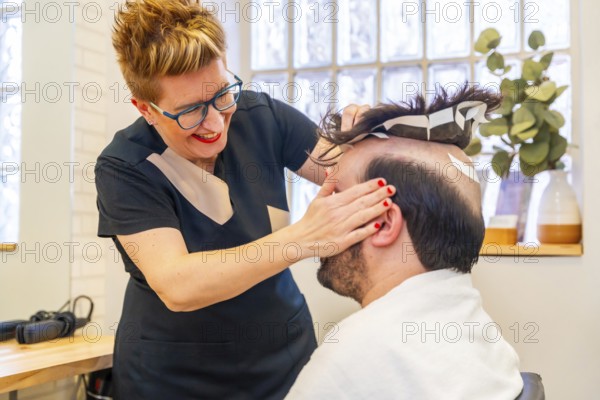 Hairdresser attaching a new capillary prosthesis to a man using adhesive stripes