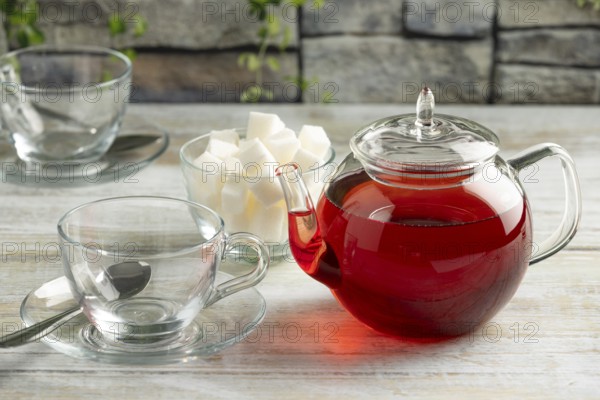 A teapot with red tea next to empty glass cups and sugar cubes on a table against a stone background