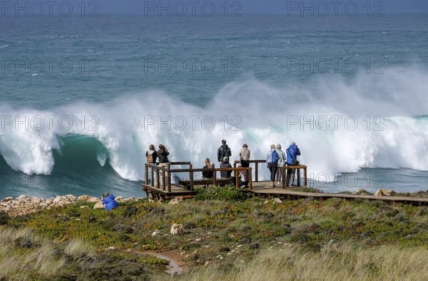 Carrapateira, Algarve, Portugal - Tourists on a viewing platform marvel at the roaring surf and spray not far from Praia do Bordeira on a stormy spring day. Carrapateira is a village in the municipality of Bordeira in the south of Portugal. It is located in the Parque Natural do Sudoeste Alentejano e Costa Vicentina, Southwest Alentejo and Costa Vicentina nature park Park