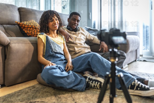 Two content creators recording a video blog in their living room using a camera on tripod