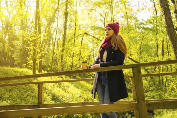 Young man with a black jacket, scarf and red woolen hat enjoying in an autumn park