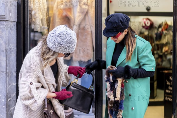Young blonde girl shopping in the city and served by a shop assistant, looking at shop windows of clothing stores. Sunglasses and red gloves
