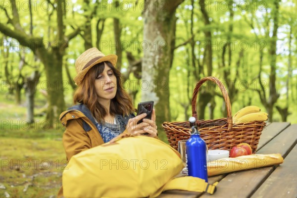 A young Caucasian mother looking at her cell phone sitting at a picnic table in the woods. Summer lifestyle