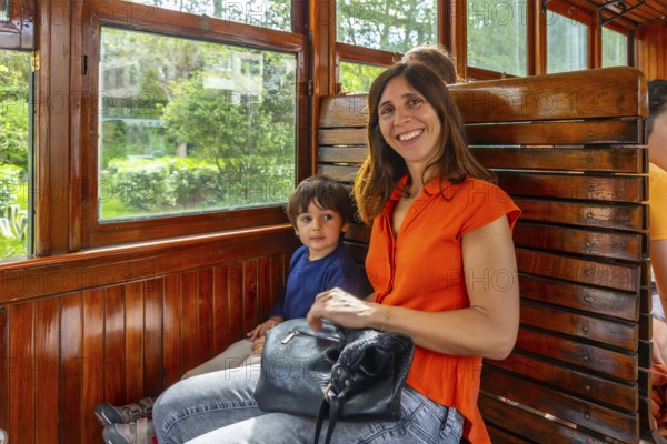 A woman and a child are sitting on a train. The woman is smiling and holding a purse