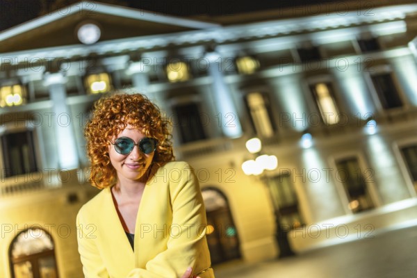 Flirty modern woman with sunglasses looking to camera standing in the city at night