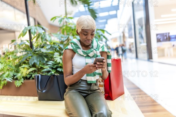 Frontal portrait of a urban stylish african woman using mobile sitting on a shopping mall