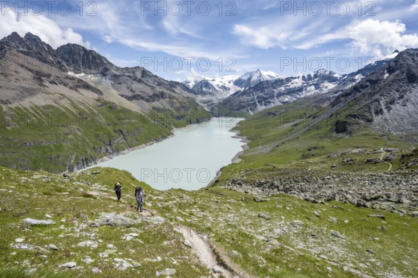 Two mountaineers on a hiking trail, view of a blue mountain lake, Lac des Dix reservoir, mountain peak Mont Blanc de Cheilon in the background, Hérménence, Valais Alps, Valais, Switzerland, Europe