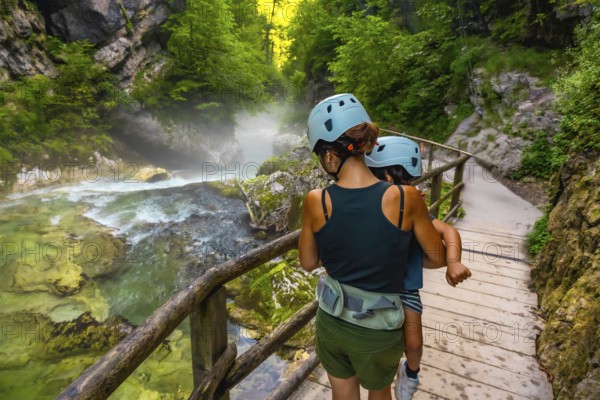Mother carrying her child while walking on a wooden pathway, exploring the scenic beauty of vintgar gorge near bled, slovenia