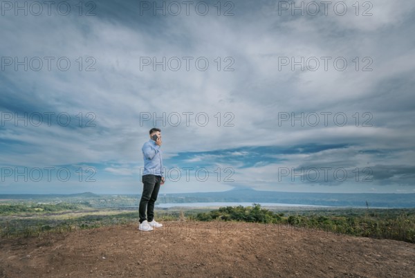 Young man talking on the phone at a viewpoint surrounded by nature. Man talking on the phone at a natural viewpoint in Masaya, Nicaragua, Central America