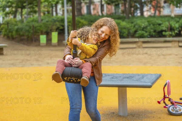 Caucasian adult mother ready to push a girl on swing in a park