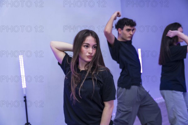 Group of young dancers practicing a modern choreography in a dance studio illuminated by purple neon lights