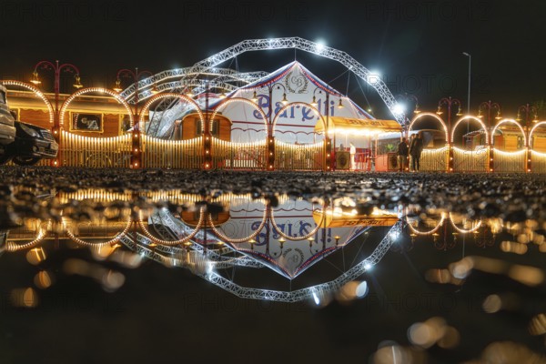 Nocturnal circus reflected in a pool of water, with illuminated arches and lights, Böblingen, Germany, Europe