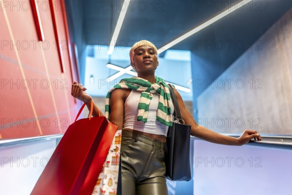 Low angle view portrait of a stylish african woman with short hair coming down an escalator carrying shopping bags