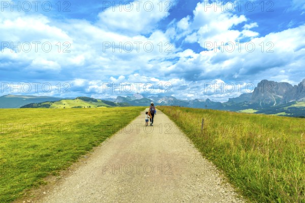 Mother and son walking on gravel path at alpe di siusi enjoying summer landscape in the dolomites, italy