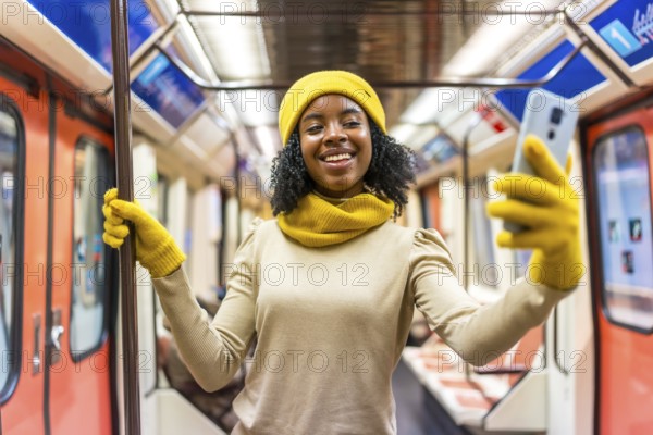 Smiling young woman wearing yellow winter accessories takes a selfie with smartphone while commuting on a subway train