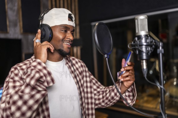 Young man wearing headphones and holding smartphone, recording a song or rap music in a professional studio
