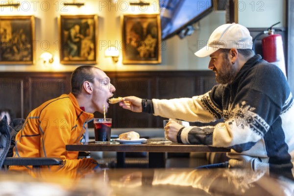 Heartwarming moment of friendship as a man helps his disabled friend enjoy a meal at a restaurant, emphasizing inclusion and support