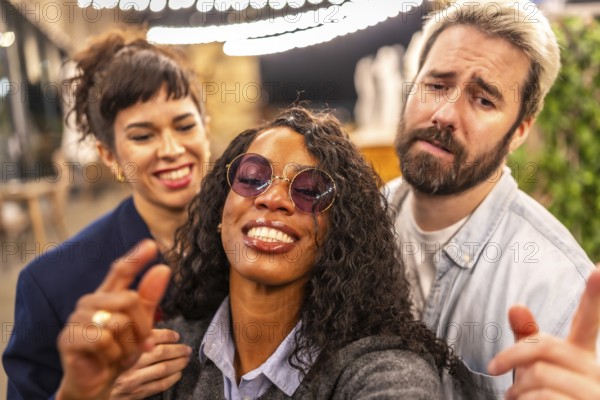 Close-up and personal point of view of multi-ethnic friends pulling funny faces while taking selfie in night party outdoors