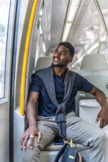 Vertical photo of a happy african entrepreneur sitting on the metro looking through window