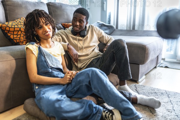 Young black couple relaxing on floor and sofa in living room, holding hands and enjoying time together