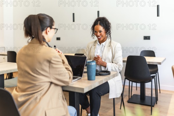 Two businesswomen are working together on a project in a modern office space, using a laptop and discussing ideas