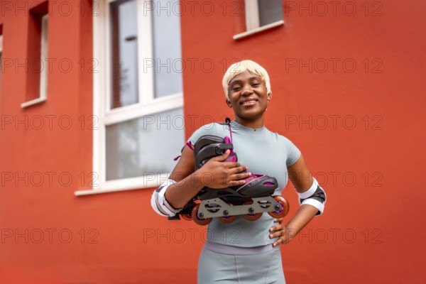 Portrait of african female skater with inline skates on shoulder standing outdoors next to red building