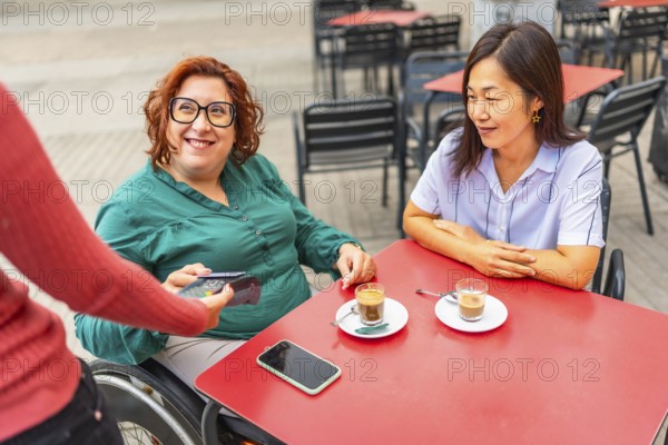 Woman with disability and asian friend paying with credit card in a sidewalk cafeteria