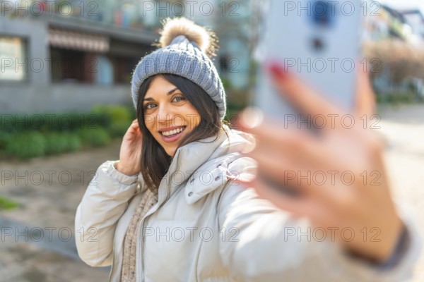 Beauty woman smiling while taking selfie with smartphone standing outdoors in a sun winter day