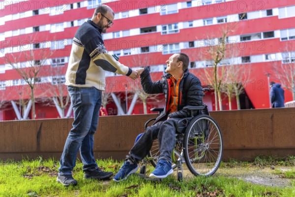 Two friends shaking hands in a city park, one of whom is using a wheelchair, demonstrating support and inclusion