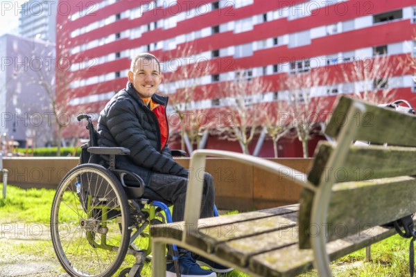 Portrait of a cheerful young disabled man sitting in a wheelchair enjoying a sunny day in a city park, promoting inclusivity and accessibility