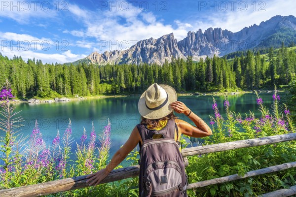 Female tourist admiring the stunning turquoise waters of lake carezza with latemar mountain range in the background, dolomites, italy