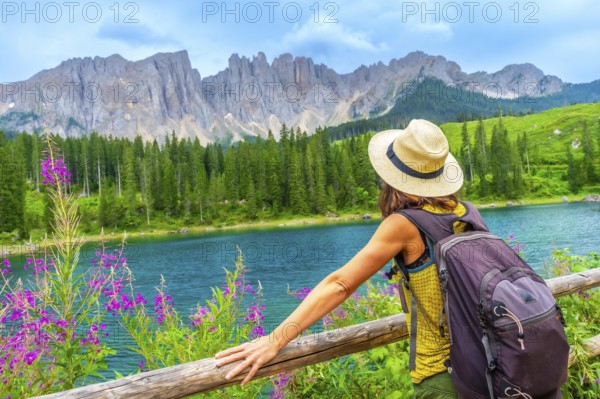 Female hiker with backpack enjoying the stunning turquoise waters of lake carezza with the latemar mountain range in the background, dolomites, italy