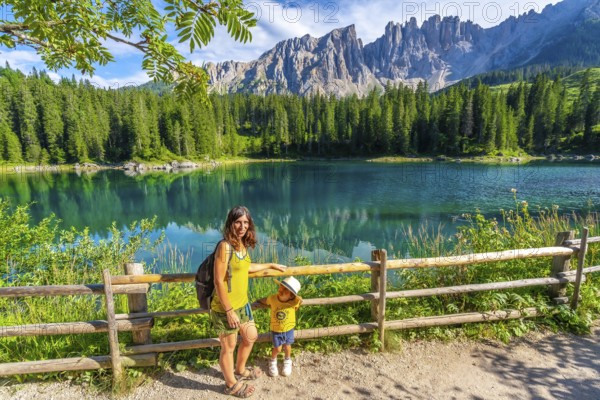 Mother and child enjoying summer holidays at the magnificent lake carezza with the latemar massif in the background, dolomites, italy