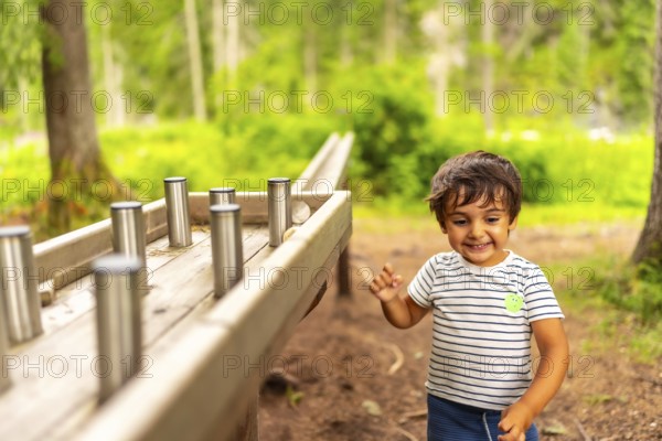 Young boy having fun interacting with a wooden sensory play table with metal cylinders in a natural forest environment, promoting learning and exploration