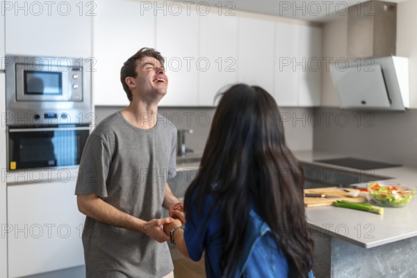 Asian woman and caucasian man sharing a joyful moment in a bright, contemporary kitchen, highlighting everyday life and cultural diversity