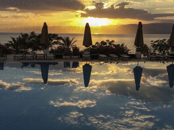 Sunset illuminated Red Sea and clouds Altostratus closed parasols reflected in swimming pool, Aqaba, Jordan, Asia