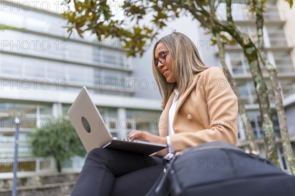 Side view low angle of a latin confident businesswoman using laptop sitting in city bench