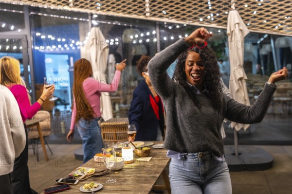 Latin woman dancing happily while partying with diverse friends in a roof bar at night