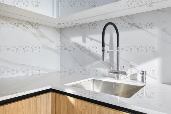 A contemporary kitchen showcases a stylish sink integrated into smooth marble countertop. The minimalist design includes elegant cabinetry and modern fixtures, offering a clean aesthetic