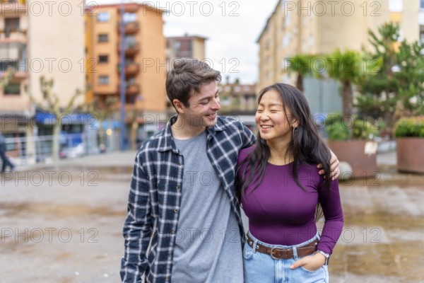 Multiethnic couple walks arm in arm, sharing a joyful moment in an urban setting. The scene captures a blend of cultures and happiness