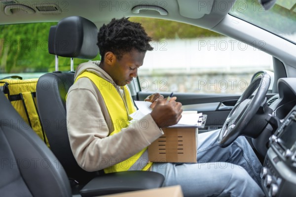 African delivery man checking packages for delivery sitting inside a car