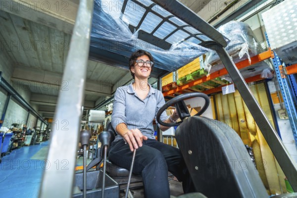 Happy female manual worker using forklift in a warehouse of a cnc metallurgic factory