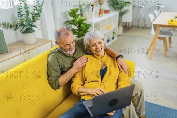 Elevated view photo of a casual senior couple lying on the sofa relaxed using laptop
