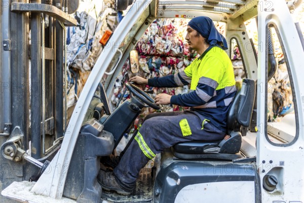Side view full length photo of a latin man worker moving plastic bales driving forklift in a recycling plant