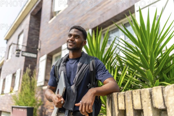 Portrait of a confident young african entrepreneur holding laptop waiting next to residential building